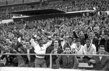 Pelé celebrando una victoria junto a un público en unas gradas. Algunos espectadores tienen caras de decepción, otros sonríen y festejan.